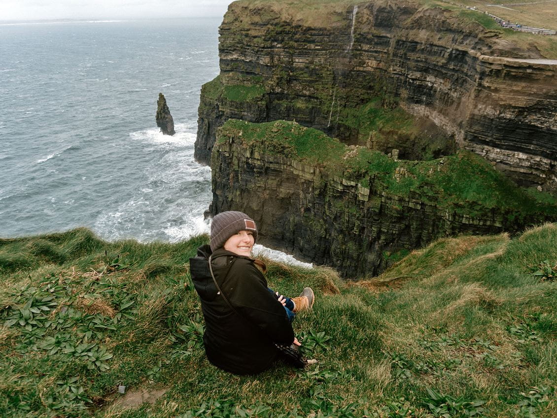 Female student sitting on the Cliffs of Moher smiling back at the camera