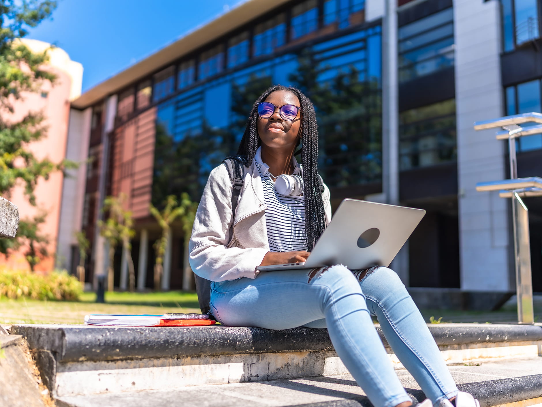 A high school-aged girl sitting on the steps outside with her laptop