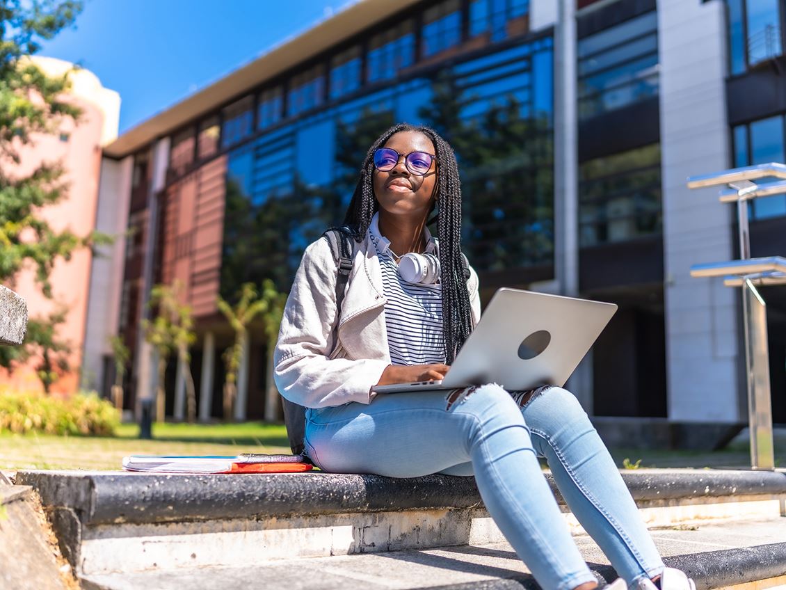 A high school-aged girl sitting on the steps outside with her laptop