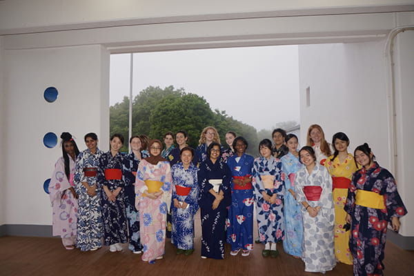 A group of young women indoors posing in colorful, patterned yukatas and sashes.