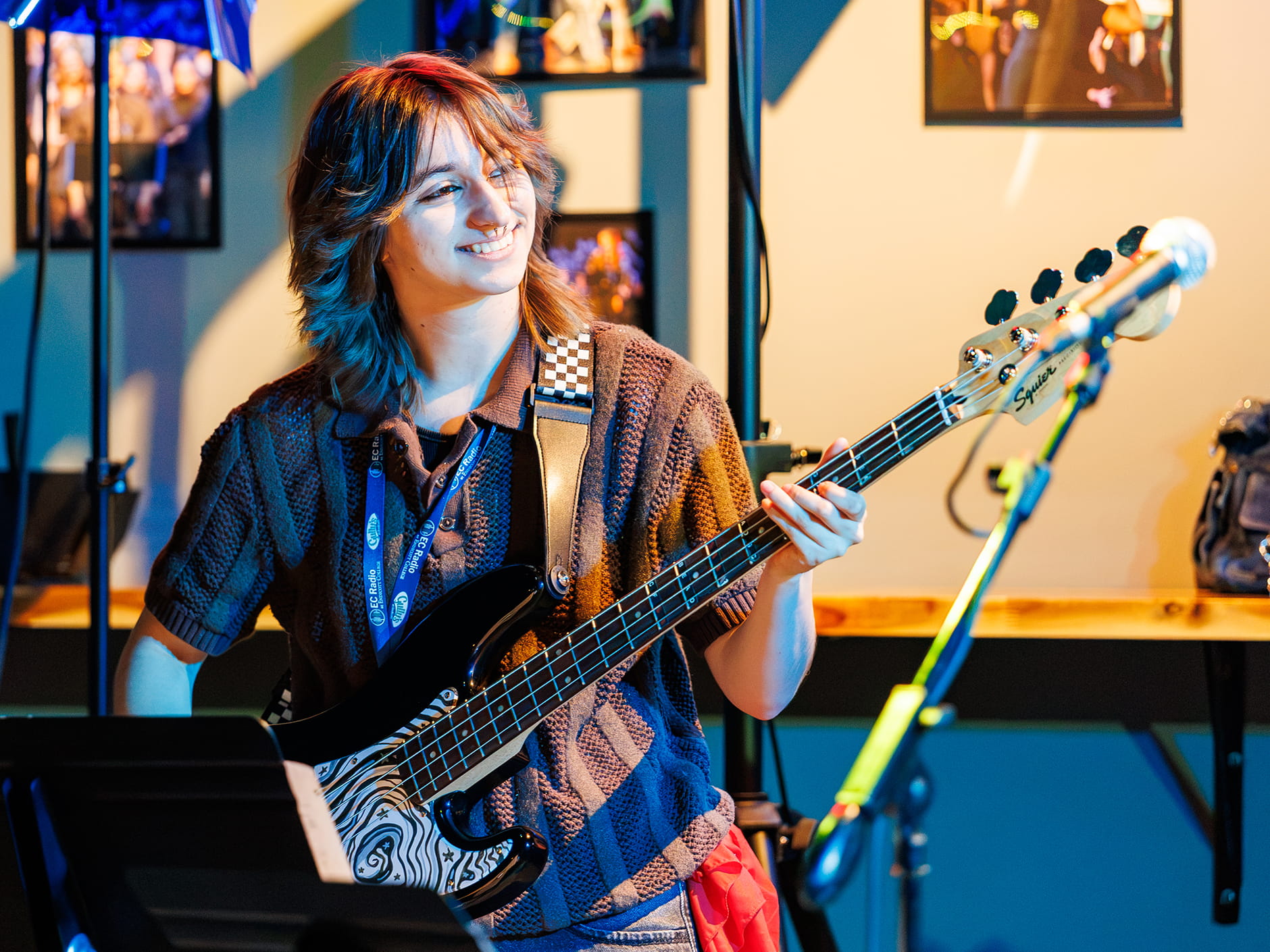A smiling student musician plays a black electric bass guitar.