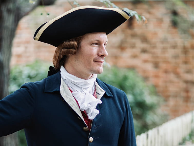 A man in 18th-century colonial attire, including a tricorn hat and white cravat, looks right.