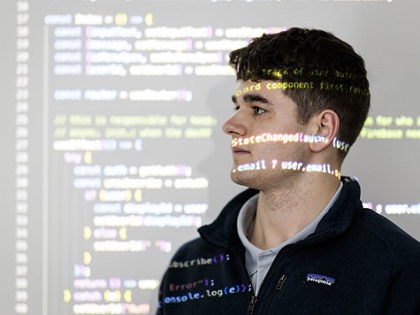 A young man looking forward with computer code projected across his face and background.