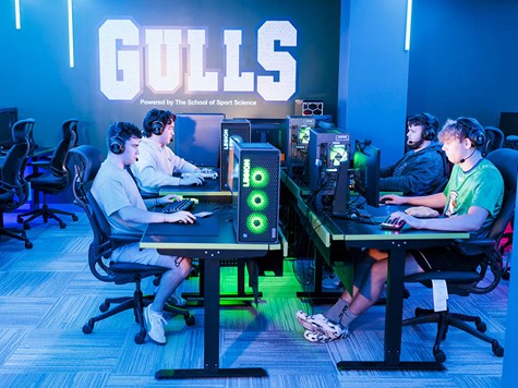 Gamers wearing headsets seated at computer stations lit up in blue neon light.
