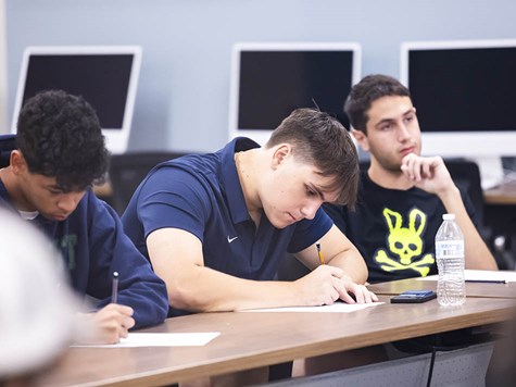 Students sitting at desks in a classroom attentively taking notes during a lecture.
