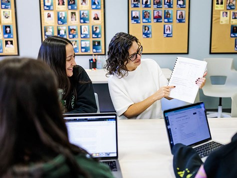 A group of female students sitting around a table reviewing printed material together.