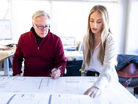 A male instructor and female student reviewing detailed architectural floor plans together.