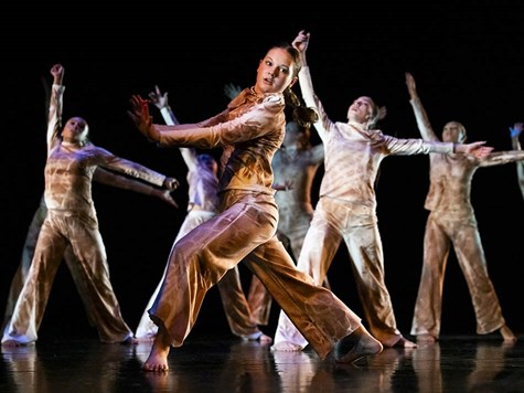 A group of dancers wearing matching earth-toned outfits performing a expressive routine on stage.